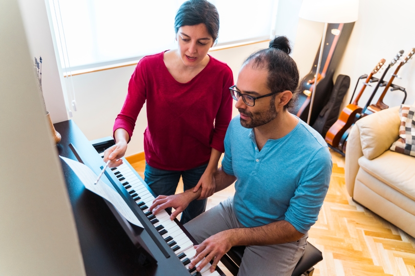 Professeure donnant un cours particulier de piano à un adulte dans un environnement convivial avec des instruments en arrière-plan