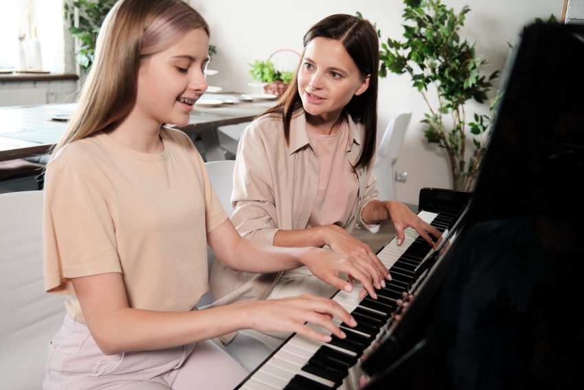 Professeure de piano enseignant à une jeune élève dans un cadre chaleureux et lumineux, illustrant un cours particulier de piano en Suisse